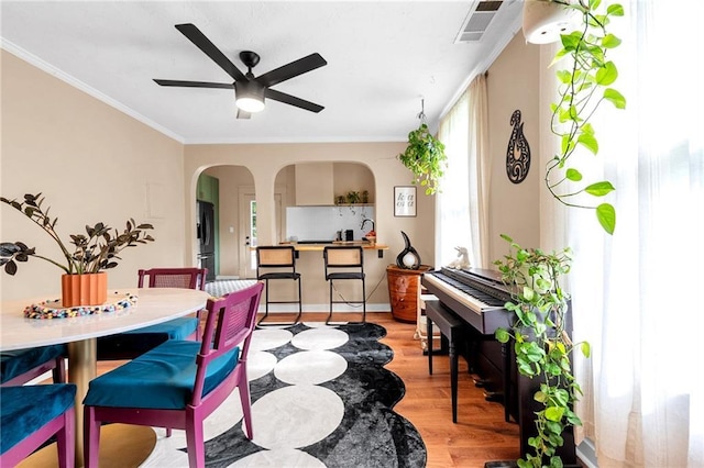 dining space with arched walkways, ceiling fan, light wood-style flooring, crown molding, and baseboards