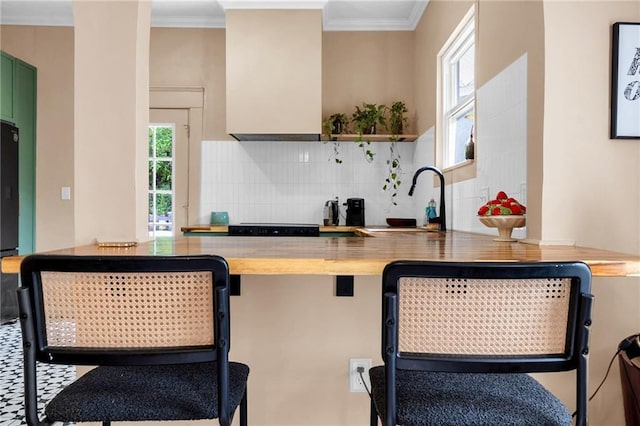 kitchen with decorative backsplash, a sink, green cabinets, crown molding, and a breakfast bar