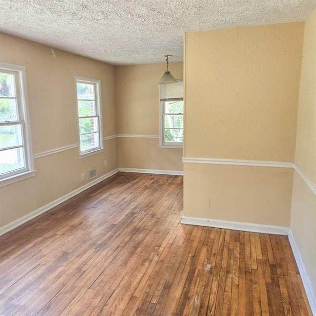 empty room featuring plenty of natural light, a textured ceiling, and hardwood / wood-style floors