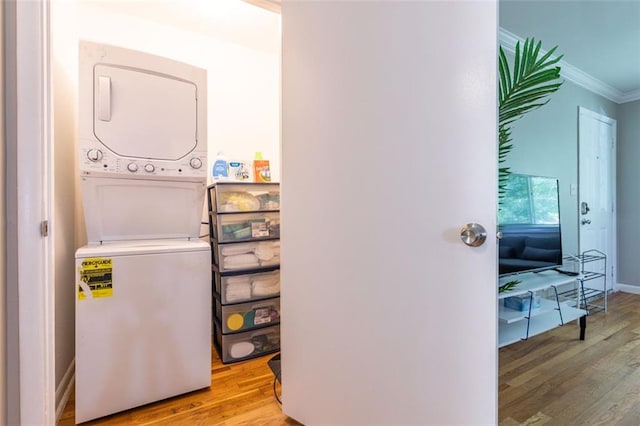 laundry room with crown molding, baseboards, laundry area, wood finished floors, and stacked washer / drying machine