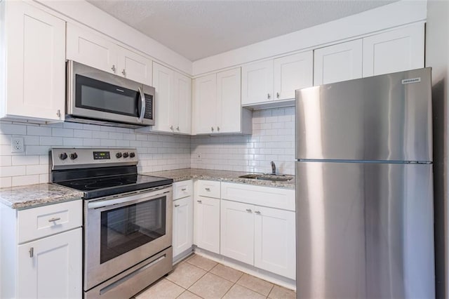 kitchen featuring a sink, appliances with stainless steel finishes, light tile patterned flooring, and white cabinets