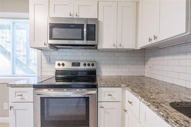 kitchen with tasteful backsplash, white cabinetry, stainless steel appliances, and light stone countertops