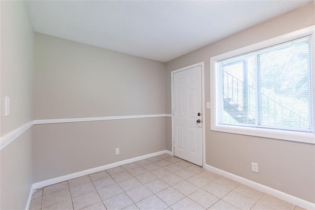 spare room featuring light tile patterned floors, baseboards, and a textured ceiling