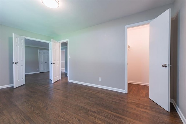 unfurnished bedroom with dark wood finished floors, a walk in closet, baseboards, and a closet