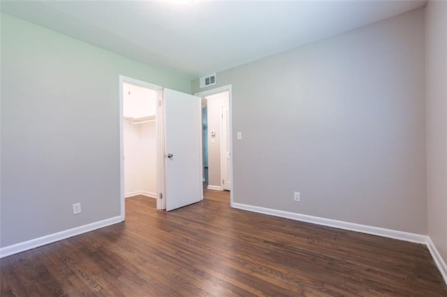 unfurnished bedroom featuring visible vents, dark wood finished floors, a closet, baseboards, and a spacious closet