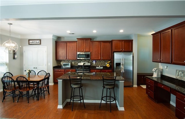 kitchen featuring appliances with stainless steel finishes, dark wood-type flooring, a breakfast bar area, a kitchen island with sink, and ornamental molding