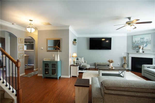 living room with arched walkways, ceiling fan, ornamental molding, stairway, and a fireplace with flush hearth