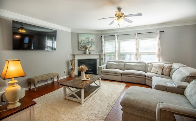 living area with ceiling fan, ornamental molding, wood finished floors, baseboards, and a glass covered fireplace