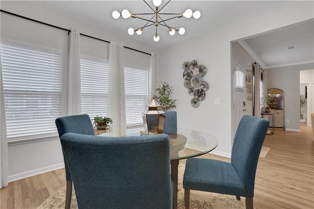 dining room with a notable chandelier, crown molding, light wood-type flooring, and baseboards