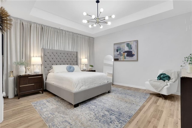 bedroom featuring an inviting chandelier, a tray ceiling, wood finished floors, and baseboards