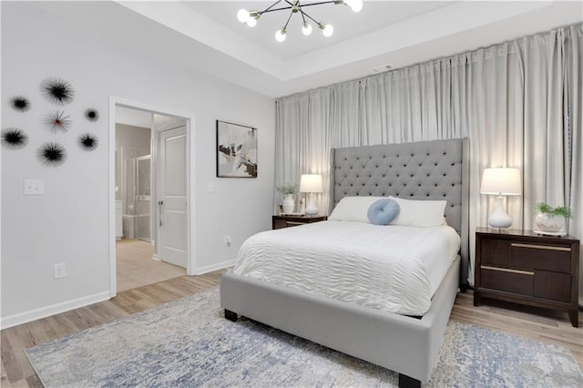 bedroom featuring wood finished floors, baseboards, ensuite bathroom, a raised ceiling, and a chandelier