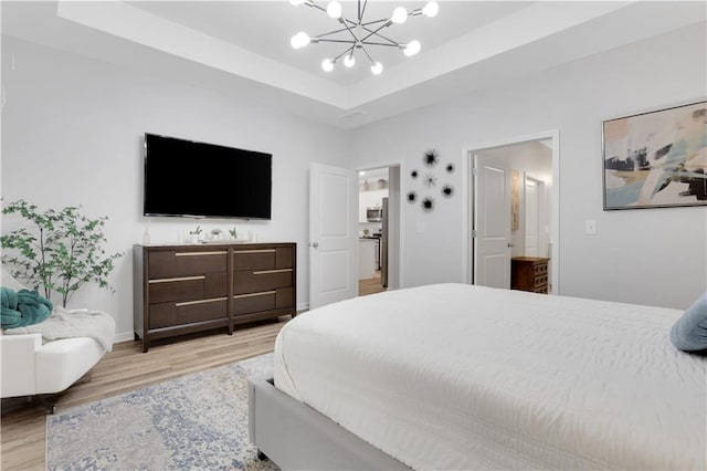 bedroom featuring light wood finished floors, baseboards, a raised ceiling, and an inviting chandelier