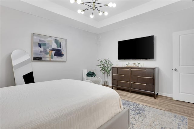 bedroom featuring baseboards, a raised ceiling, an inviting chandelier, and wood finished floors