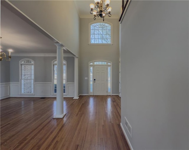 entryway with dark wood-style floors, crown molding, visible vents, an inviting chandelier, and ornate columns