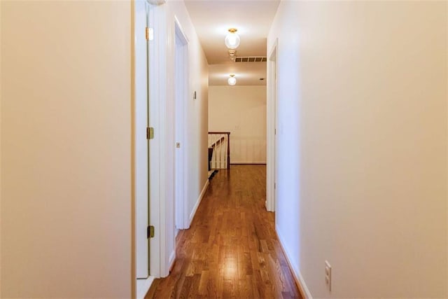 corridor with visible vents, baseboards, an upstairs landing, and wood finished floors