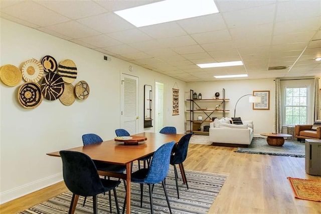 dining area featuring visible vents, a drop ceiling, baseboards, and wood finished floors
