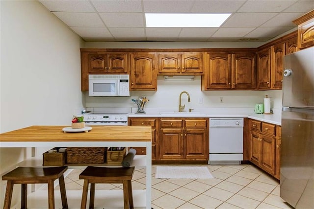 kitchen featuring white appliances, a drop ceiling, light countertops, a sink, and brown cabinets