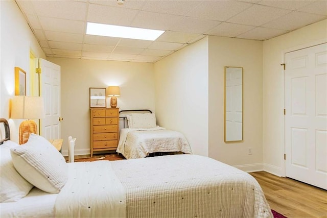 bedroom with baseboards, a paneled ceiling, and wood finished floors