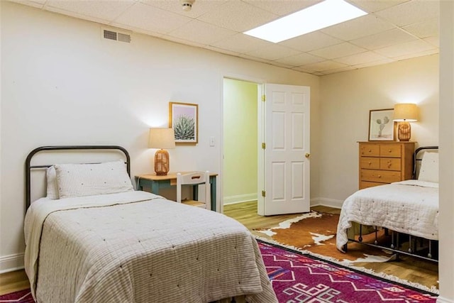 bedroom featuring visible vents, baseboards, a paneled ceiling, and wood finished floors