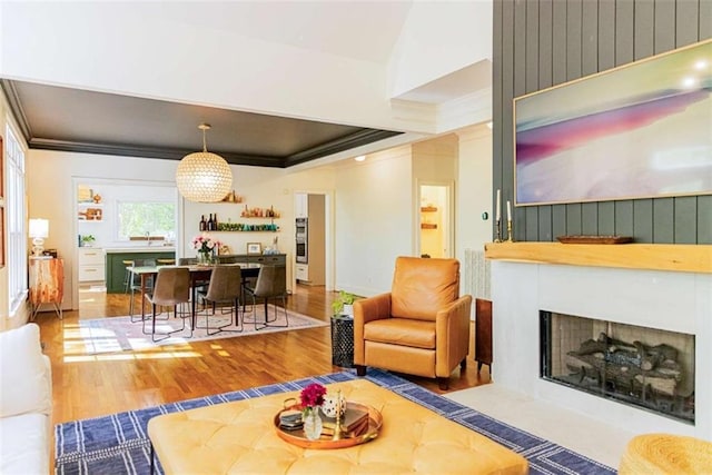 living area with a fireplace with flush hearth, crown molding, and wood finished floors