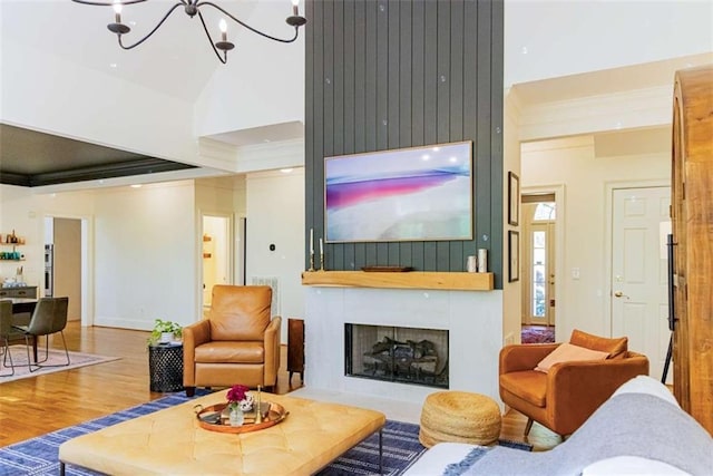 living area with an inviting chandelier, a large fireplace, ornamental molding, wood finished floors, and lofted ceiling