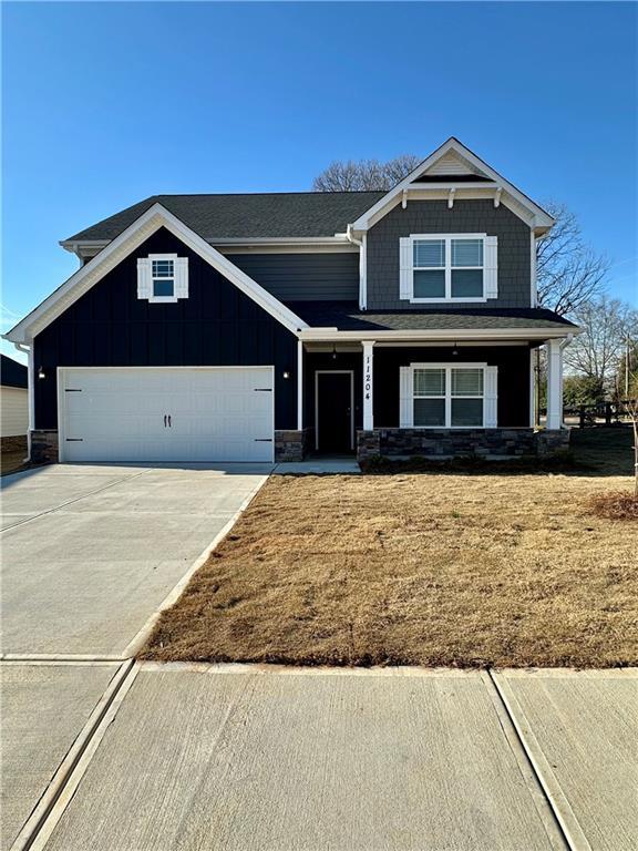 craftsman-style home with board and batten siding, concrete driveway, stone siding, and a front lawn