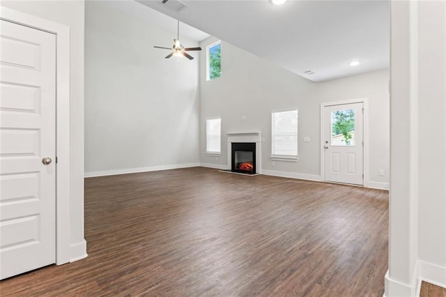unfurnished living room with visible vents, dark wood finished floors, a glass covered fireplace, and ceiling fan