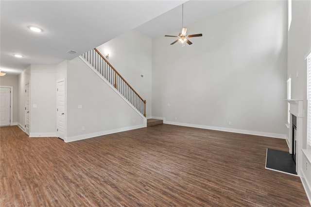 unfurnished living room with a ceiling fan, dark wood-style flooring, a fireplace, stairway, and baseboards
