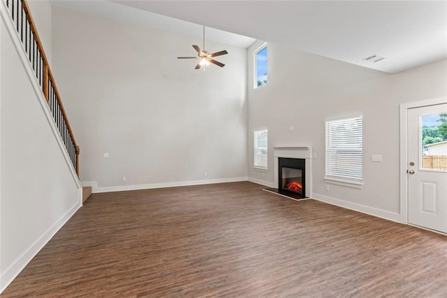 unfurnished living room featuring ceiling fan, visible vents, baseboards, dark wood-style floors, and a glass covered fireplace