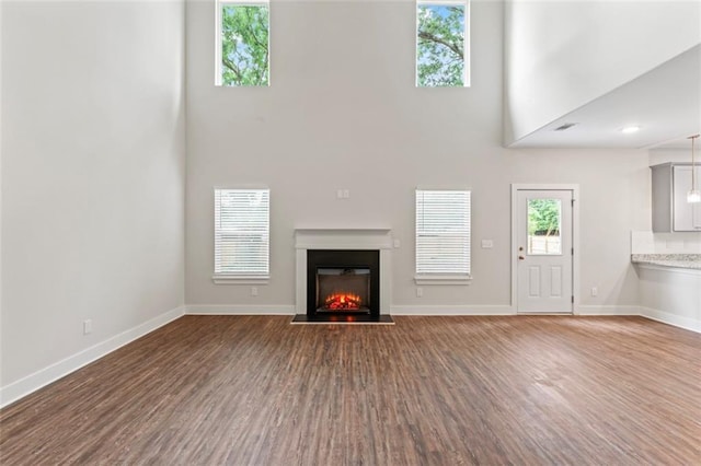 unfurnished living room featuring baseboards, a high ceiling, a glass covered fireplace, and wood finished floors