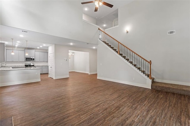 unfurnished living room featuring a ceiling fan, dark wood-style floors, stairs, and visible vents