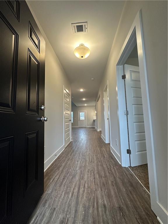 hall with baseboards, visible vents, and dark wood-style flooring