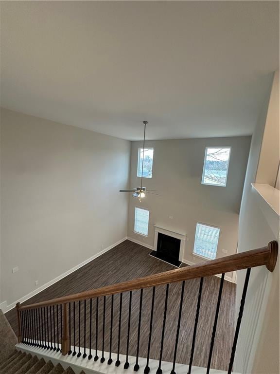 stairway with a wealth of natural light, baseboards, a fireplace with raised hearth, and ceiling fan