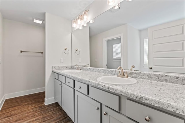 full bath with a sink, baseboards, double vanity, and wood finished floors