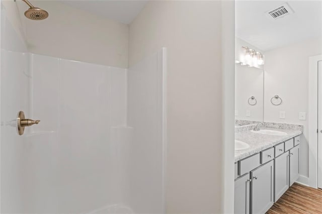 bathroom with a sink, double vanity, wood finished floors, a shower, and visible vents