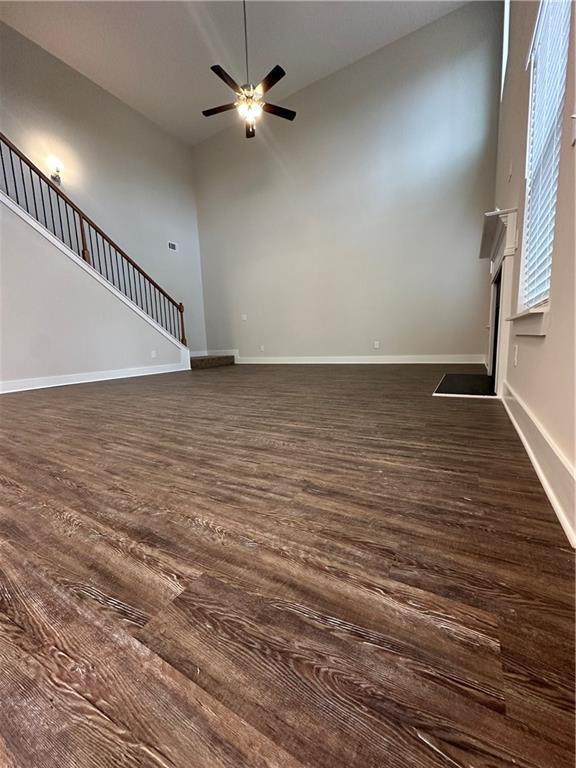 unfurnished living room with ceiling fan, baseboards, stairs, and dark wood-type flooring