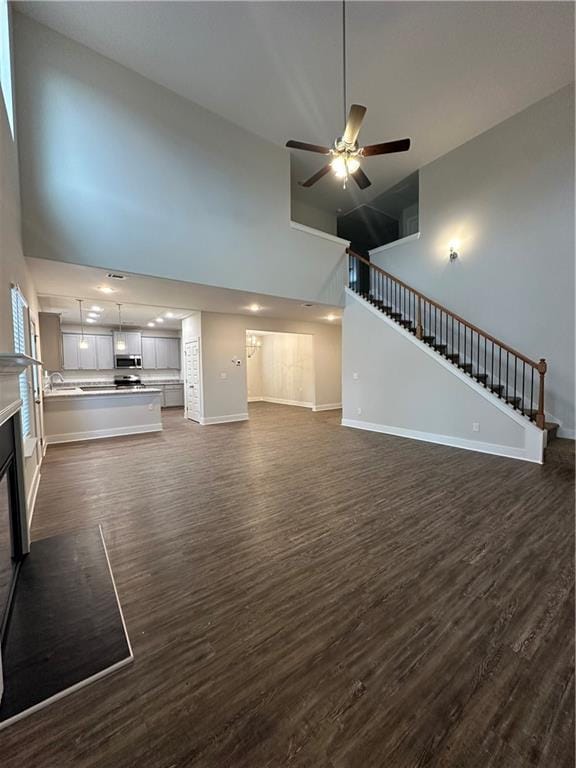 unfurnished living room featuring ceiling fan, baseboards, a towering ceiling, and stairs