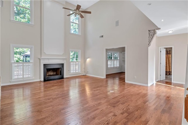 unfurnished living room featuring a high ceiling, wood-type flooring, plenty of natural light, and ceiling fan