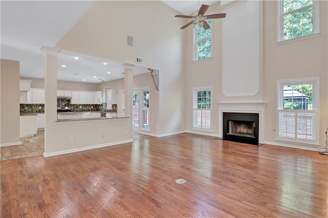 unfurnished living room with light wood-type flooring, ceiling fan, high vaulted ceiling, and ornate columns