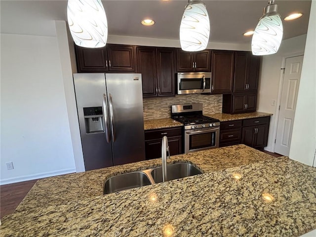 kitchen featuring backsplash, dark brown cabinetry, hanging light fixtures, stainless steel appliances, and a sink