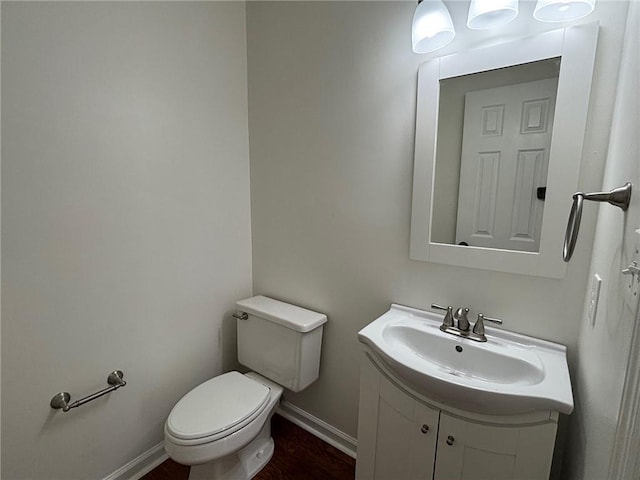 half bath featuring vanity, toilet, wood finished floors, and baseboards