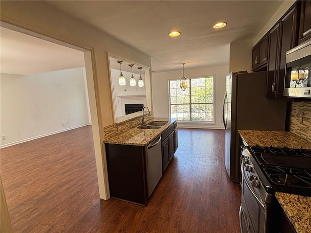 kitchen featuring stone counters, a fireplace, a sink, dark brown cabinetry, and appliances with stainless steel finishes