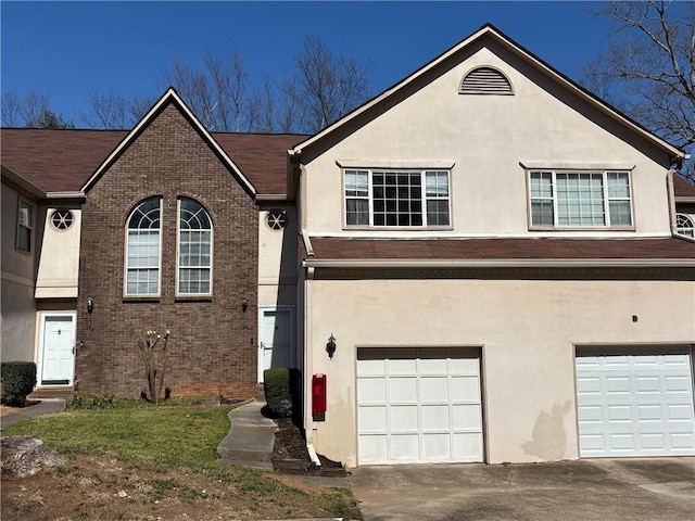 view of front of home with a garage, brick siding, driveway, and stucco siding