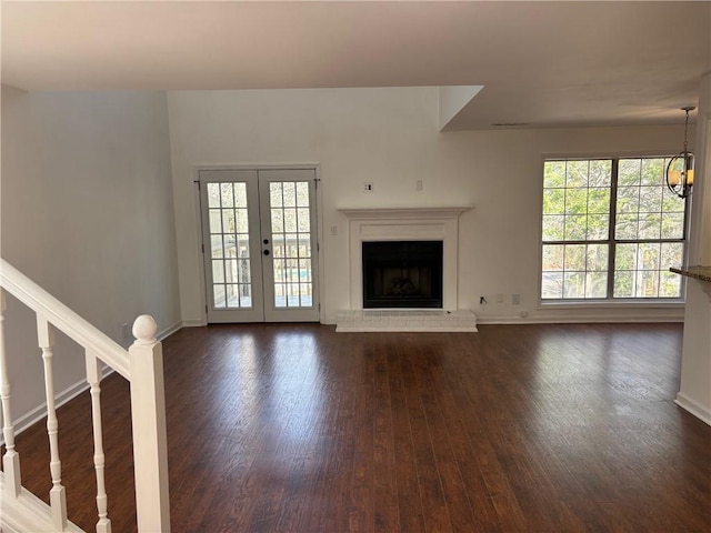 unfurnished living room featuring stairway, baseboards, dark wood-type flooring, french doors, and a brick fireplace