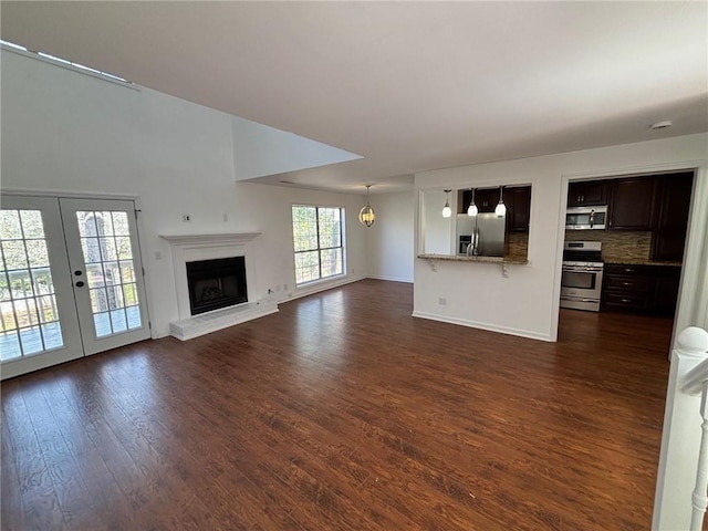 unfurnished living room featuring a fireplace with raised hearth, french doors, dark wood-type flooring, and baseboards