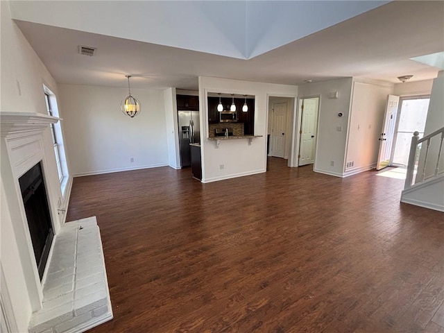 unfurnished living room featuring visible vents, dark wood-type flooring, a fireplace, baseboards, and stairs