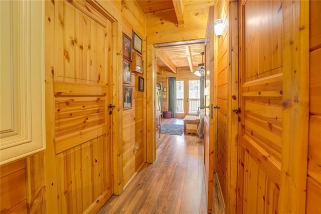 hall with beamed ceiling, wooden ceiling, hardwood / wood-style floors, and wooden walls