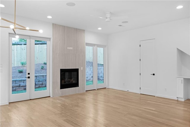 unfurnished living room featuring a large fireplace, a healthy amount of sunlight, ceiling fan with notable chandelier, and light wood-type flooring