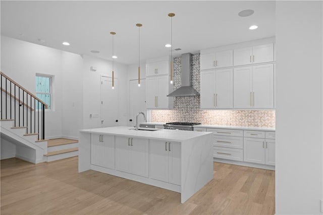 kitchen with a kitchen island with sink, sink, wall chimney range hood, decorative light fixtures, and white cabinetry