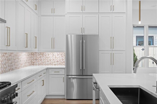 kitchen with white cabinetry, sink, tasteful backsplash, stainless steel fridge, and stove